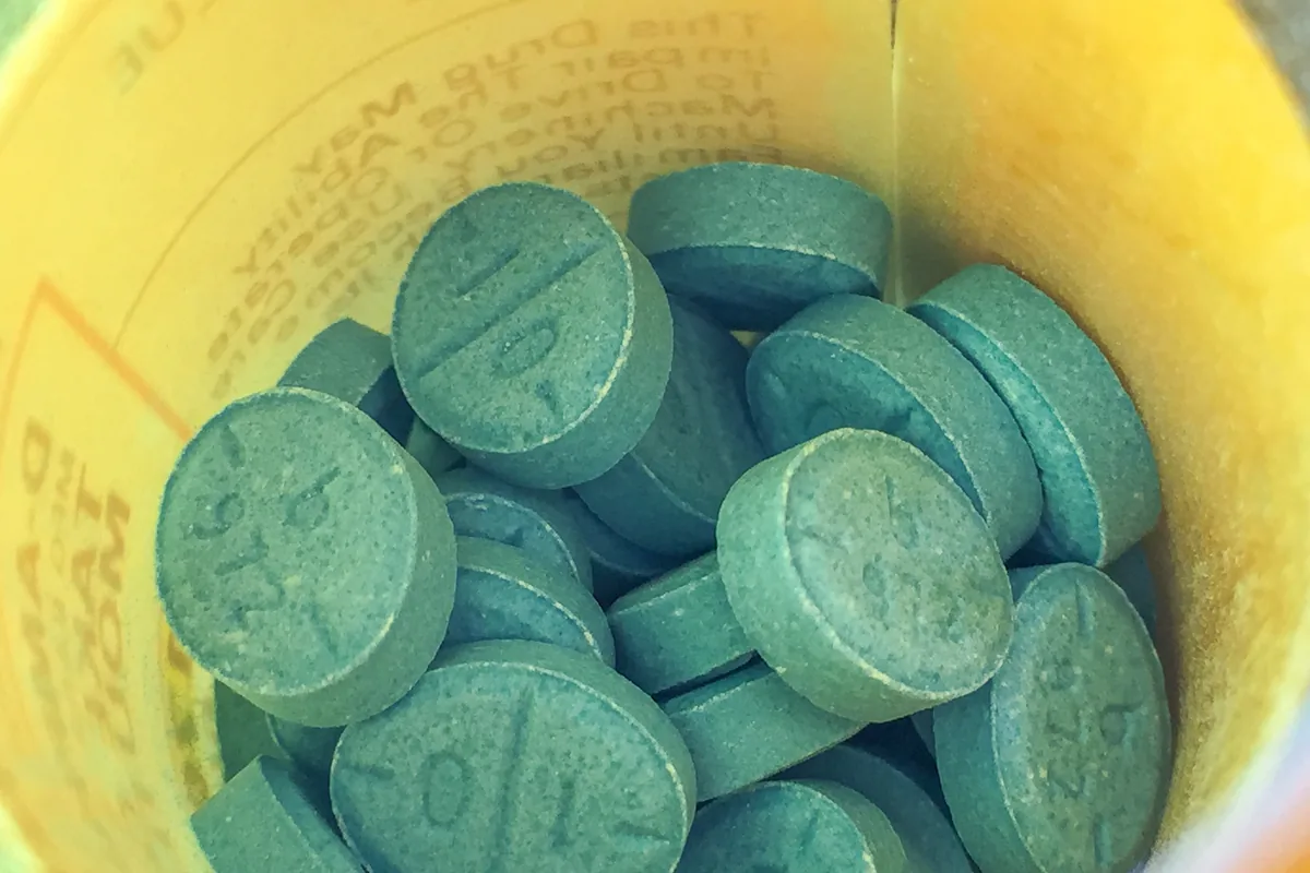 Blue Adderall tablets seen from above inside an orange pharmacy prescription vial