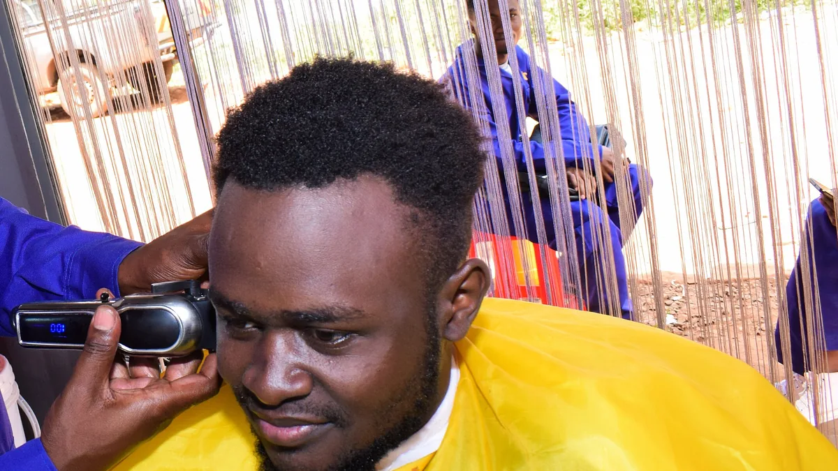 Un barbier utilise une tondeuse électrique pour couper très court les cheveux au-dessus de l'oreille d'un client, première étape d'une coupe rasée