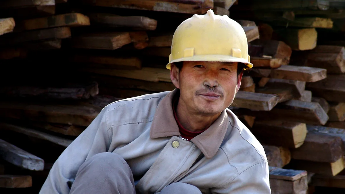 Construction worker wearing a hard hat beside a stack of timber