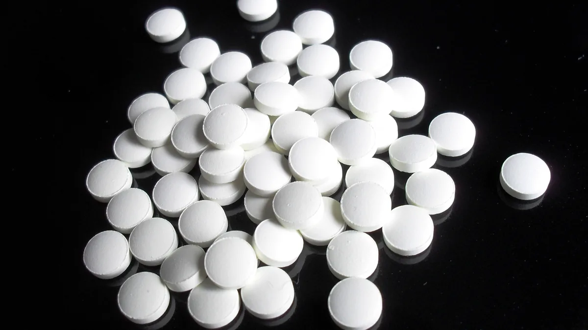 A pile of round white tablets without markings or packaging, photographed on a black surface