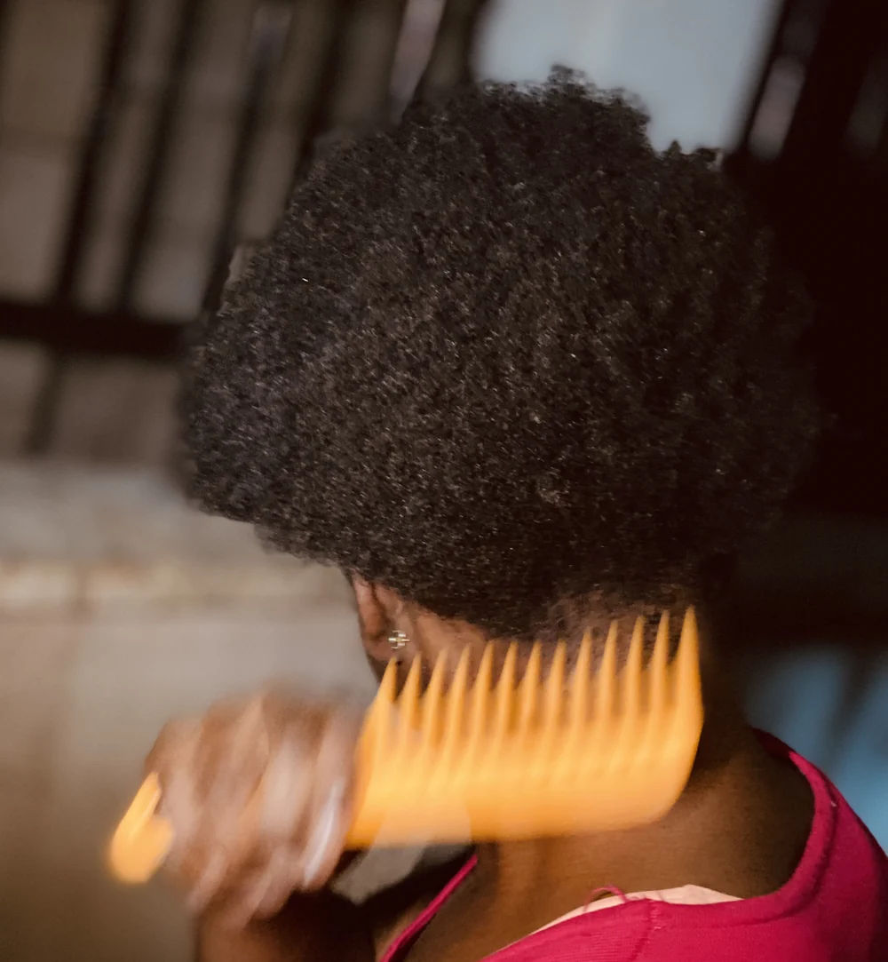 Back of a person's head as they comb Afro-textured hair with a wide-tooth comb