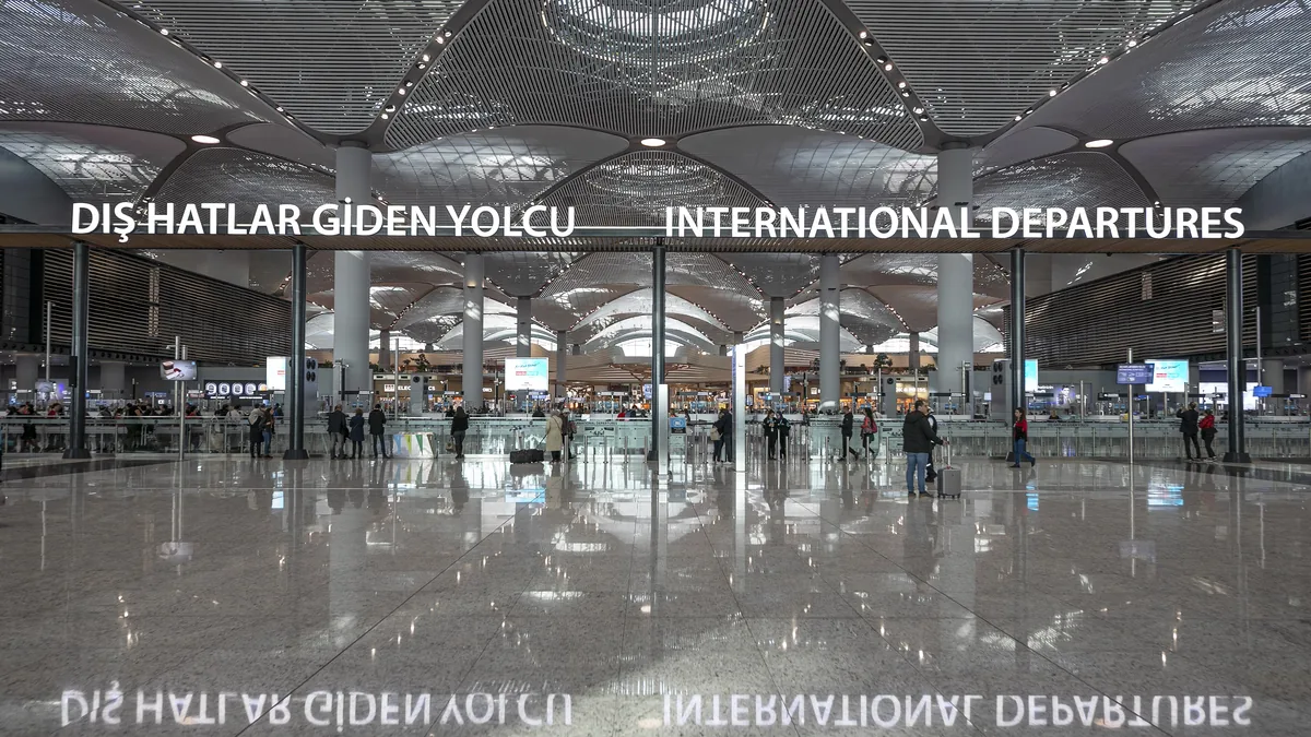 Voyageurs traversant la zone lumineuse des départs internationaux de l'aéroport d'Istanbul, sous un haut plafond blanc