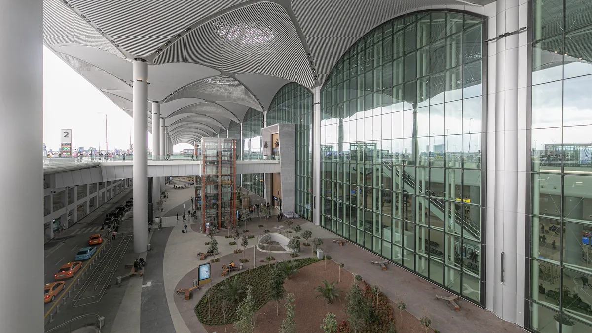 Parvis paysager et arboré vu à travers la paroi vitrée du terminal de l'aéroport d'Istanbul