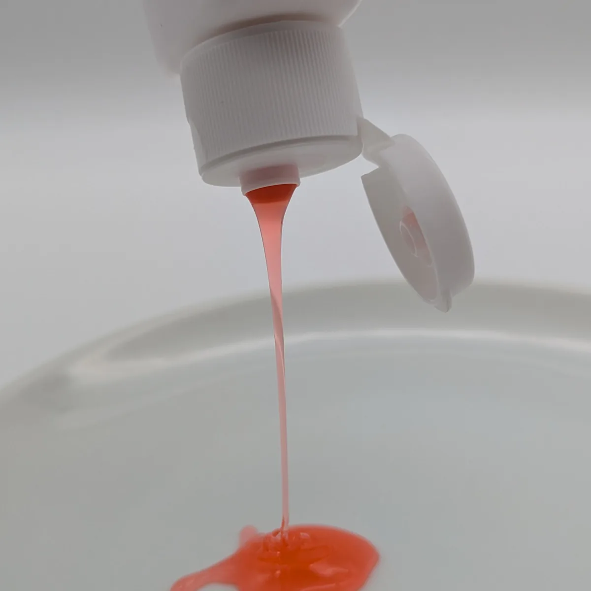 Orange-pink ketoconazole 2% shampoo being squeezed from an upturned bottle into a small pool on a white surface