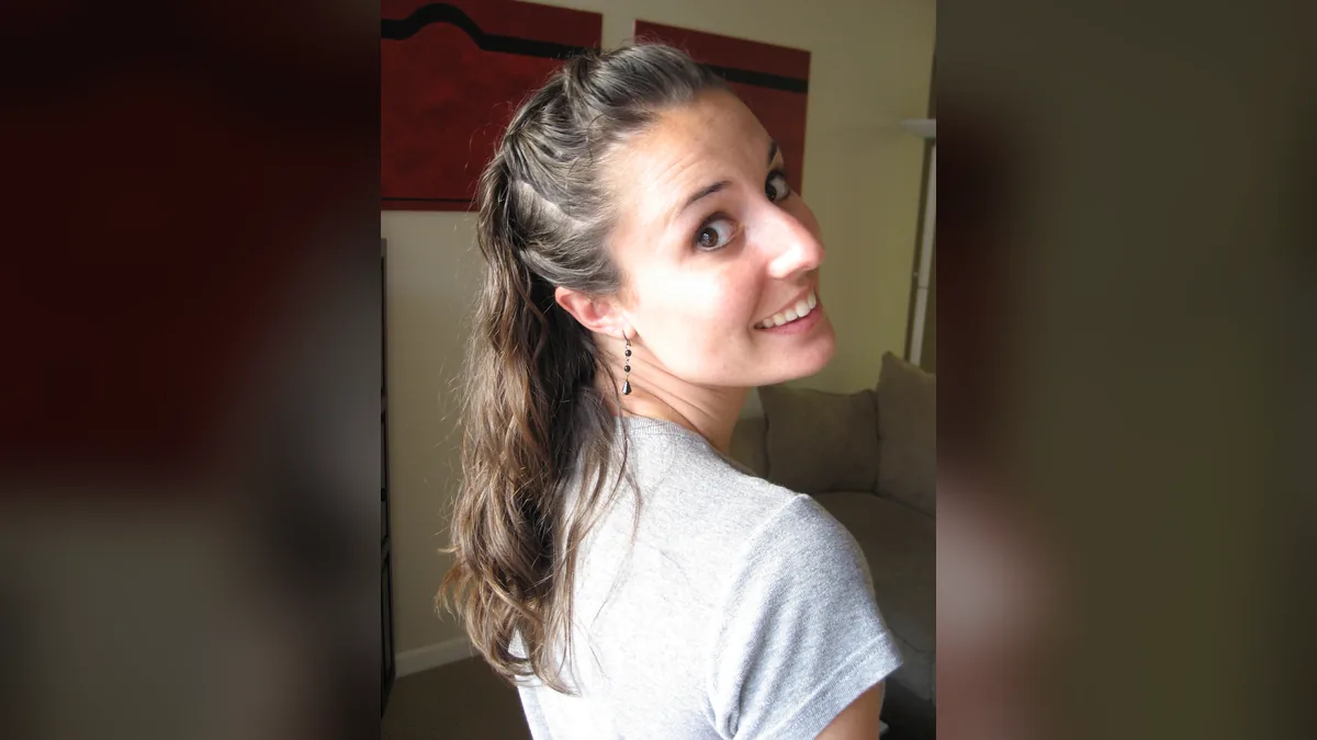Femme regardant par-dessus son épaule, cheveux bruns longs et légèrement ondulés, attachés à moitié