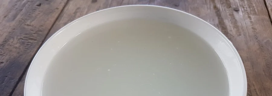 White bowl filled with cloudy rice water on a wooden table