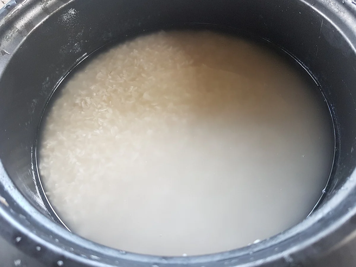Uncooked white rice soaking in cloudy water inside a dark cooking pot