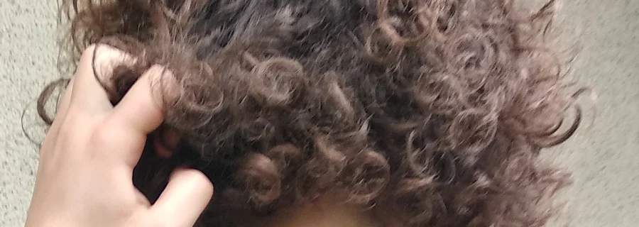 A hand twisting and pulling a lock of curly brown hair, seen from behind