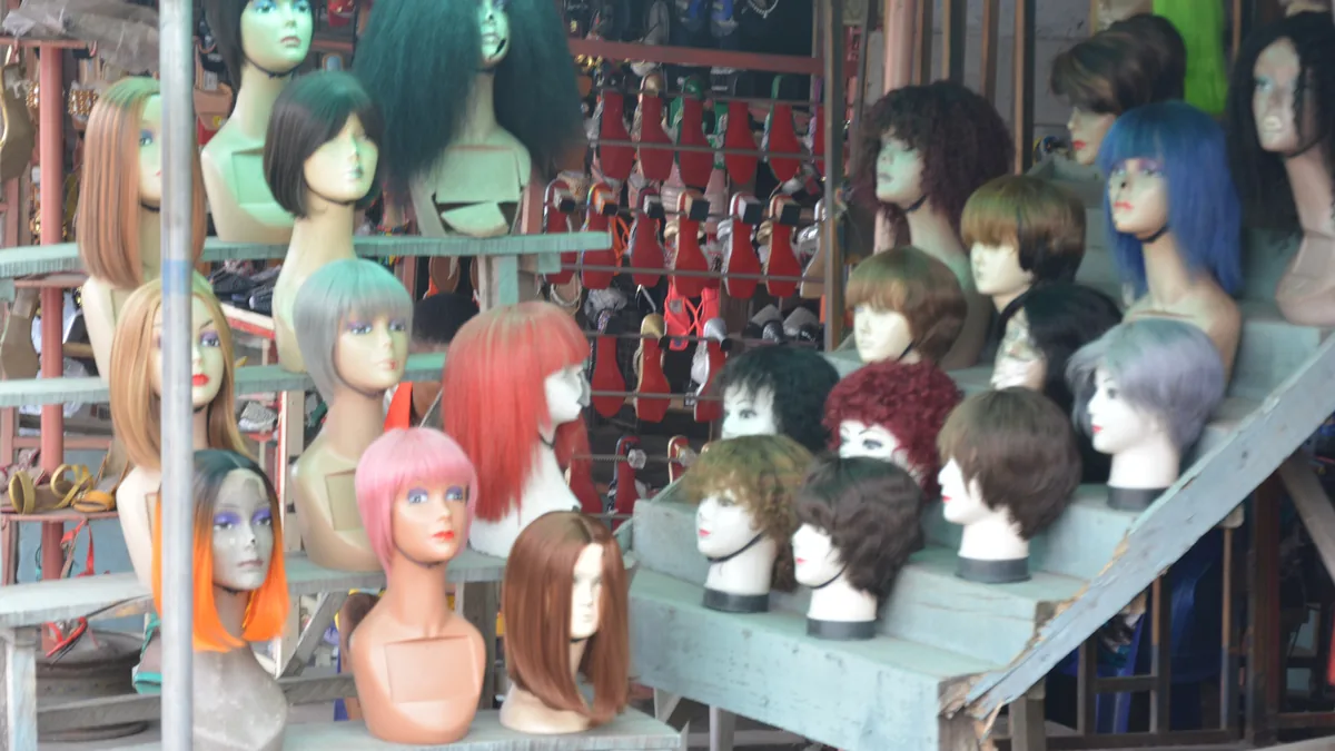 Rows of wigs in many colours and styles on mannequin heads at a market stall